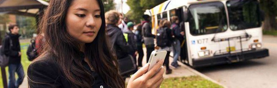 Woman looking at mobile phone as passengers board a bus.